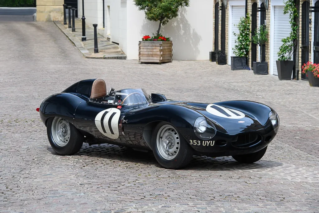 Classic black vintage race car on cobblestone street, featuring white racing numbers and sleek aerodynamic design.