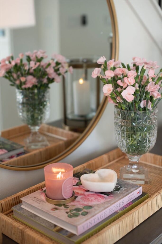 Pink flowers and a candle on a decorative tray with a mirror in a cozy, elegant interior setting.