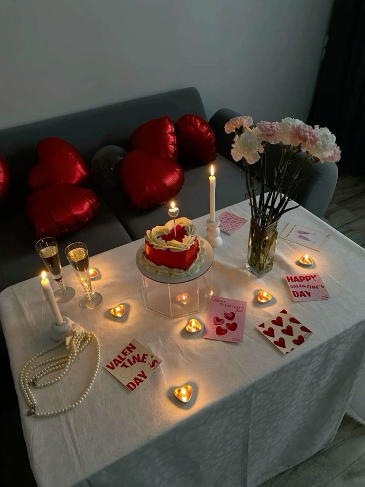 Valentine's Day celebration setup with candles, cake, flowers, heart balloons, and cards on a decorated table.