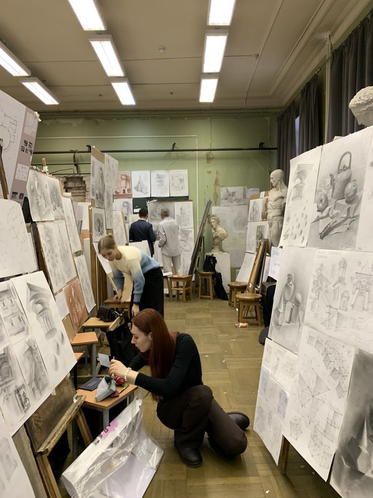 Art students working in a studio surrounded by sketches and sculptures.