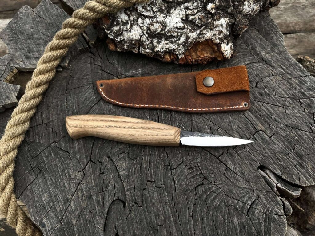 Wood-handled knife with leather sheath on rustic wooden surface, rope in view. Ideal for outdoor enthusiasts.