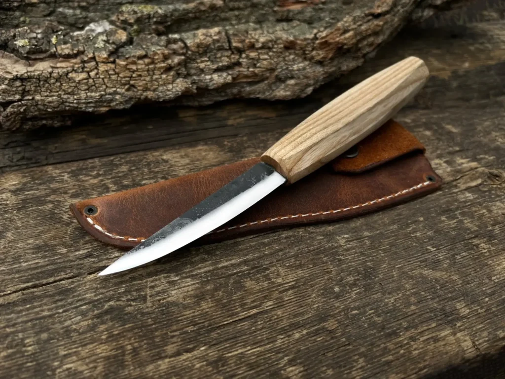 Wood-handled knife on leather sheath, rustic background. Ideal for camping or outdoor cooking.