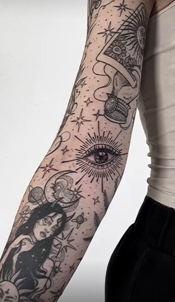 Arm with celestial and tarot tattoos, featuring an eye, moon, stars, and detailed cosmic designs.