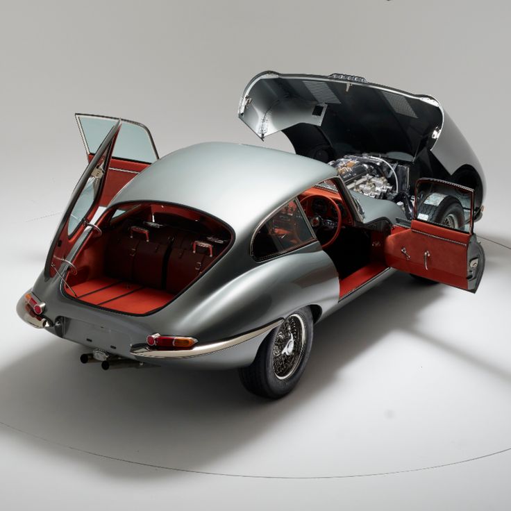 Classic vintage car with open doors and hood, showcasing elegant design and interior, in a studio setting.