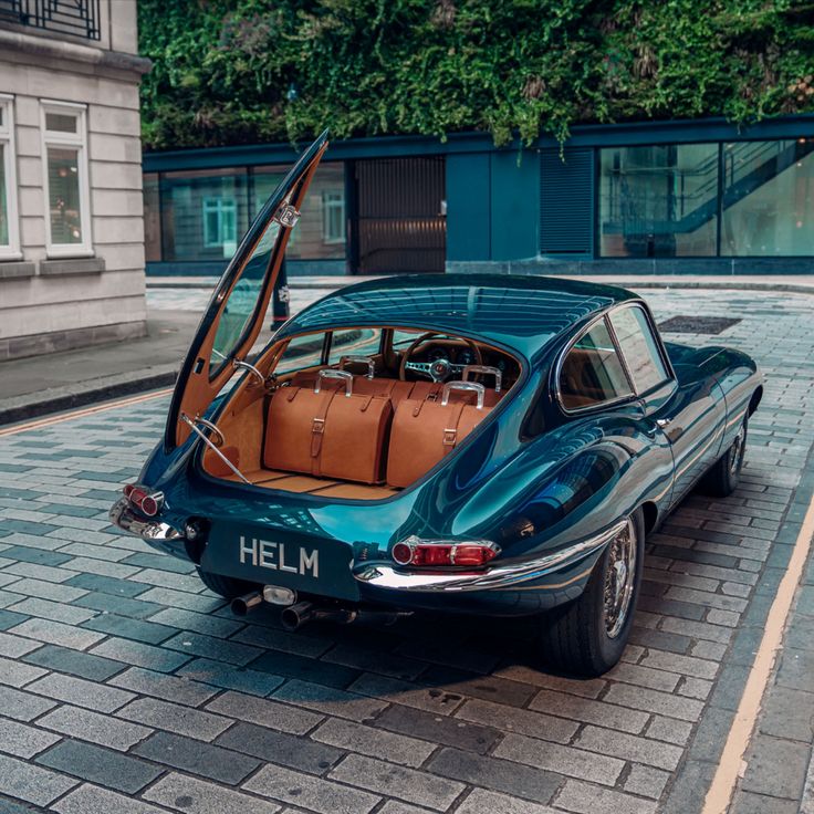 Vintage teal car with open trunk showcasing luggage on cobblestone street. Modern luxury travel concept.