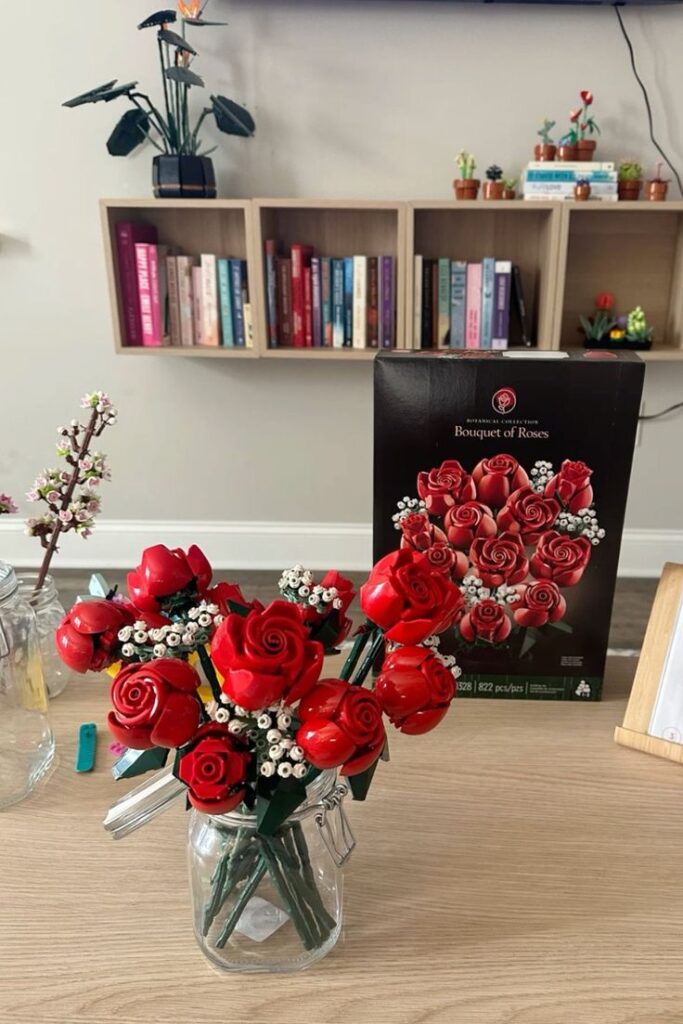 LEGO rose bouquet in a glass jar on a wooden table with bookshelves in the background.