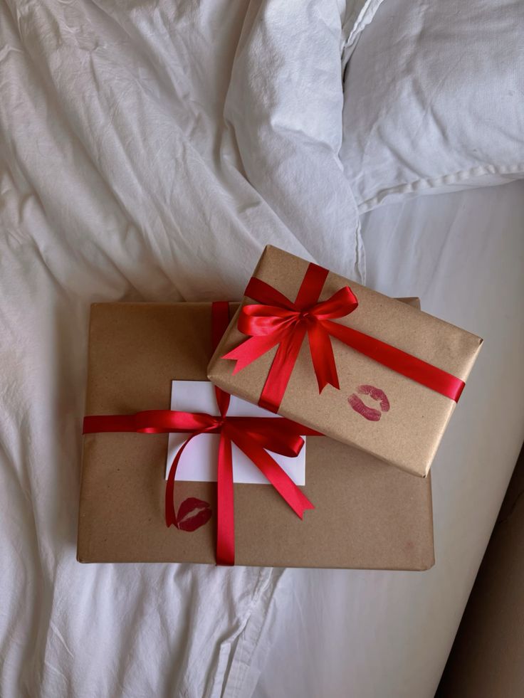 Two gift boxes with red ribbons and lipstick kiss marks, resting on a white bedsheet.