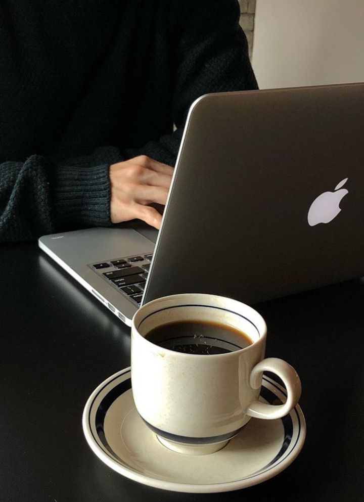 Person typing on a laptop with a cup of black coffee in the foreground on a desk.