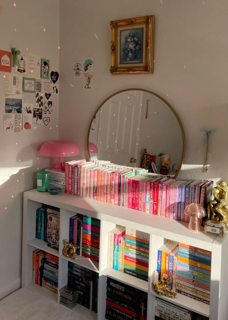 Cozy bookshelf with colorful books, decorative items, and a mirror reflecting warm sunlight on a serene wall.