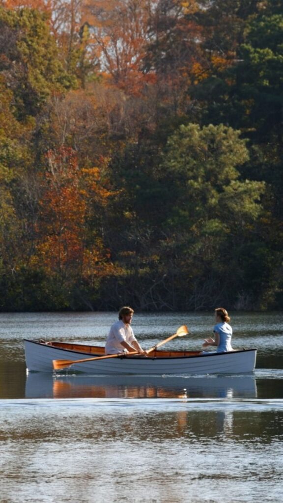 Couple rowing a boat on a lake surrounded by autumn trees, enjoying a serene and picturesque day outdoors.