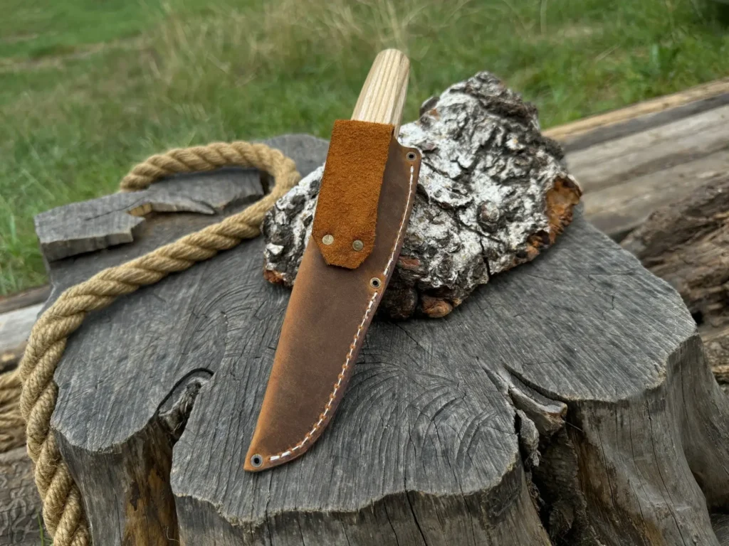 Rustic outdoor scene with a knife in a leather sheath, rope, and tree stump. Perfect for camping or wilderness themes.