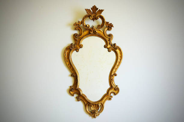 Ornate antique gold mirror with intricate floral frame design hanging on a white wall.