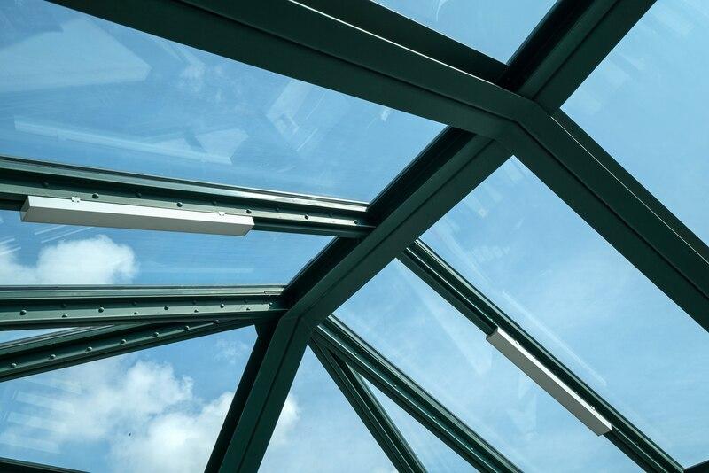 Glass ceiling with metal beams against a clear blue sky, showcasing modern architectural design.