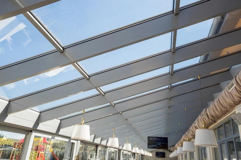 Modern glass atrium with natural light, featuring hanging lamps and scenic views through large skylights.