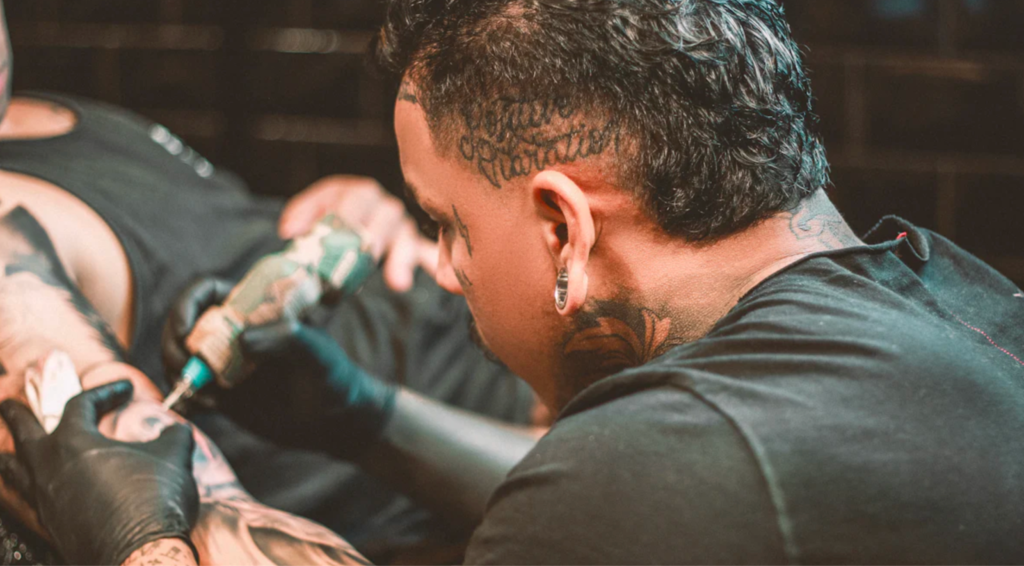 Tattoo artist inking a client's arm with precision in a studio setting.