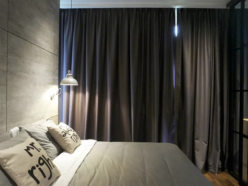 Modern bedroom with dark curtains, cozy bedding, and reading lamp. Minimalist design for a serene sleep environment.