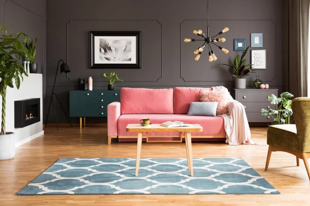 Stylish living room with pink sofa, modern chandelier, and geometric rug, creating a cozy and elegant ambiance.