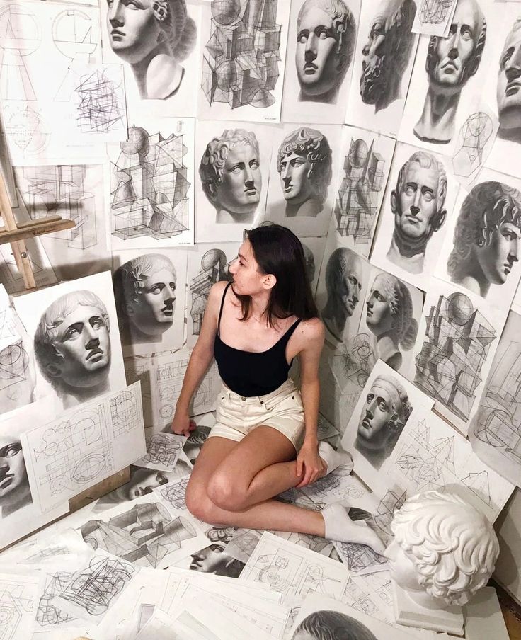 Artist surrounded by graphite sketches of classical sculptures.