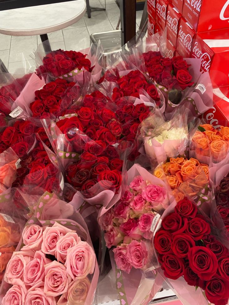 Bouquets of red, pink, and orange roses displayed alongside Coca-Cola boxes in a store.