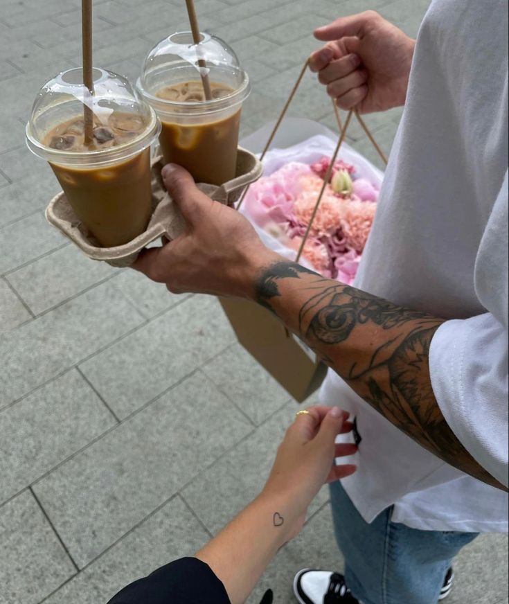 Couple holding hands, carrying iced coffees and a bouquet of flowers, showcasing a romantic outing.