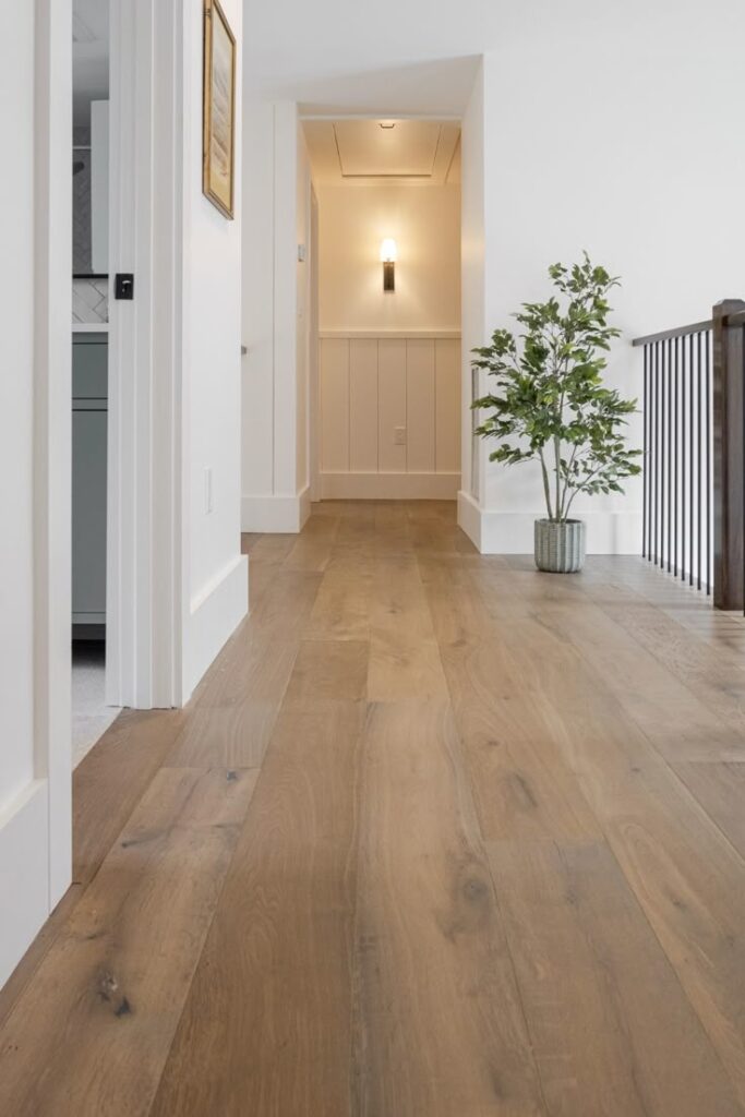 Modern hallway with light wood flooring, white walls, black railing, and a potted plant.