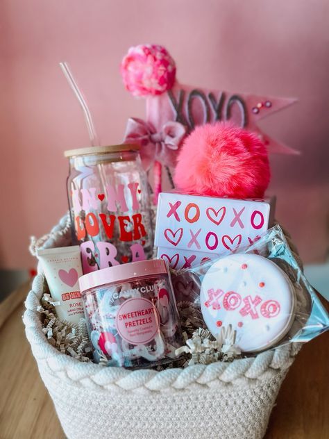 Gift basket with pink-themed Valentine treats, including a jar, sweets, and decor, on a wooden surface.