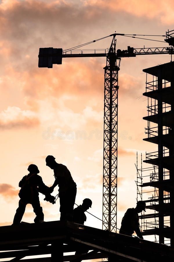 Construction workers at sunset on site with crane in background, silhouetted against orange sky.