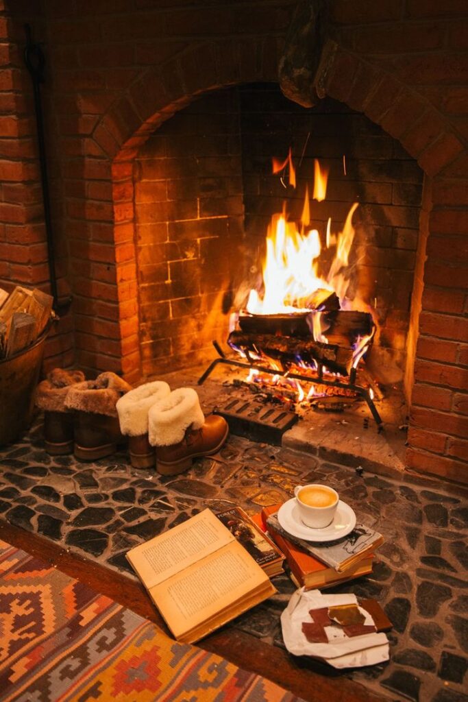 Cozy fireplace setting with fluffy boots, books, chocolate, and a cup of coffee on a warm winter evening.