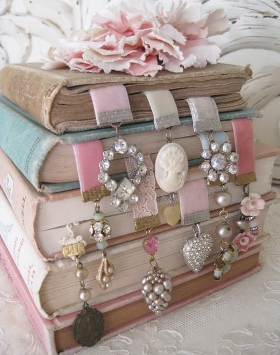 Stack of vintage books with decorative jeweled bookmarks and pink flowers on top.