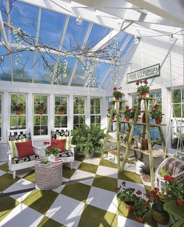 Bright sunroom with potted plants, cozy chairs, checkered floor, and floral decor under a glass ceiling. Perfect for relaxation.