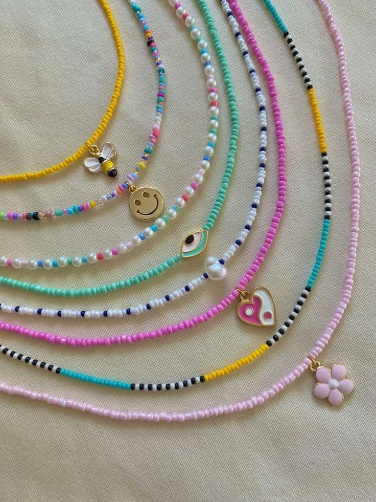 Colorful beaded necklaces with cute charms on a light background, featuring designs like bees, smiley faces, and hearts.