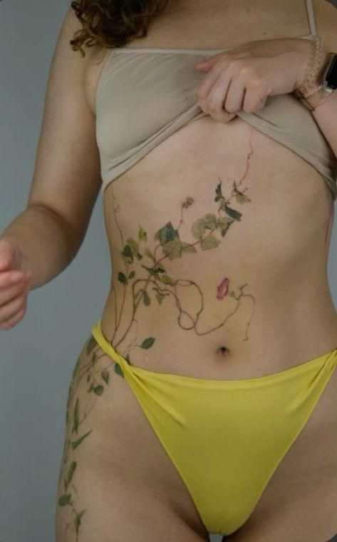 Woman with floral body art wearing a bikini, showcasing intricate vine and floral tattoo designs on her skin.