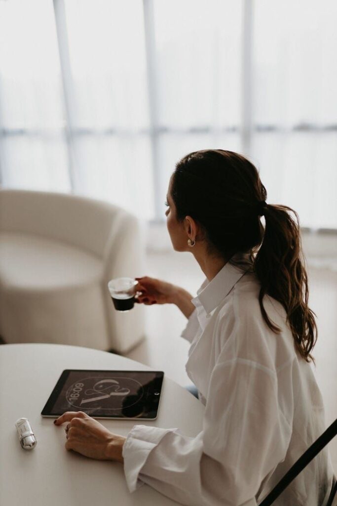 Woman with ponytail enjoying coffee, tablets on table, modern room background.