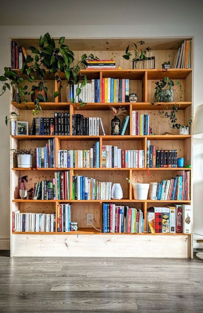 Wooden bookshelf filled with colorful books and plants, enhancing a cozy home library atmosphere.