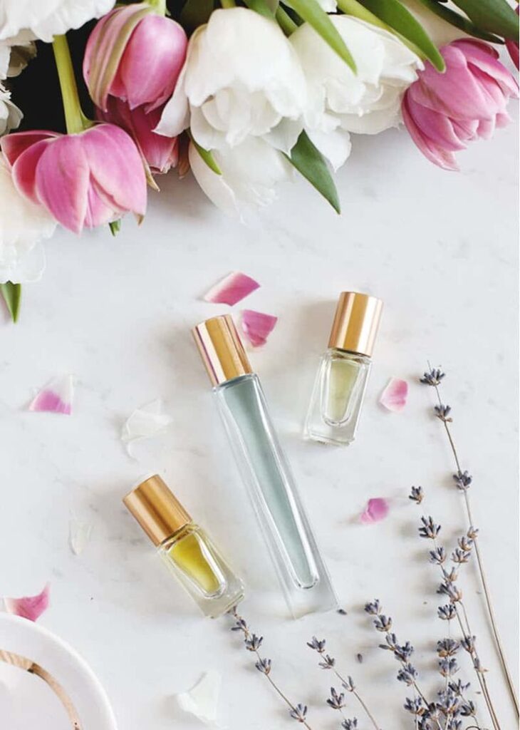 Perfume bottles with gold caps on a white surface, surrounded by pink flowers and lavender sprigs.