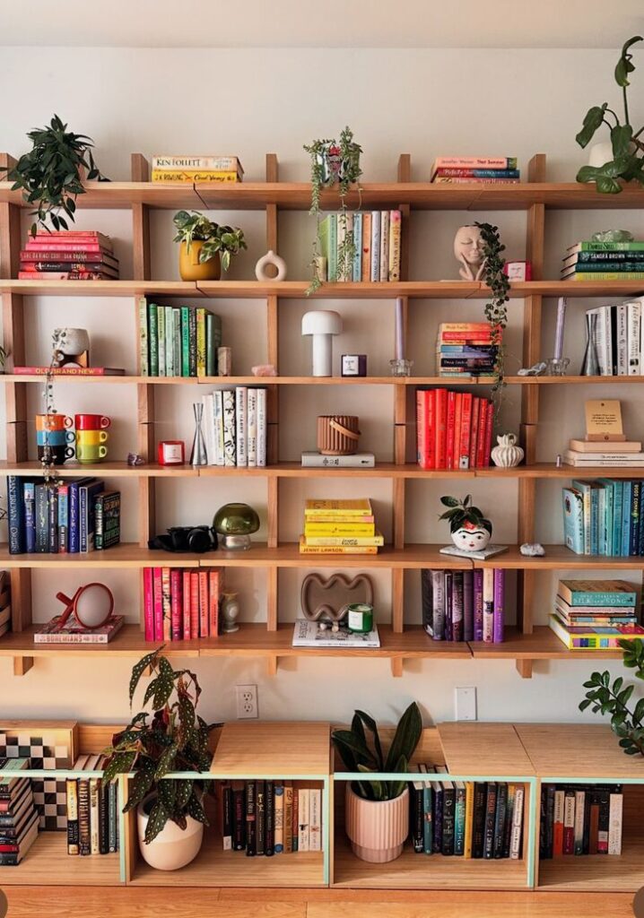 Vibrant bookshelf with books, plants, and decor on wooden shelves, creating a colorful and cozy home library.