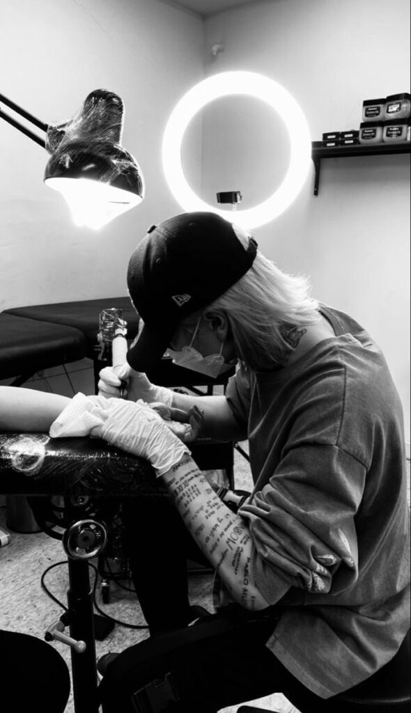 Tattoo artist at work in studio, creating intricate designs under bright light. Black and white photography.