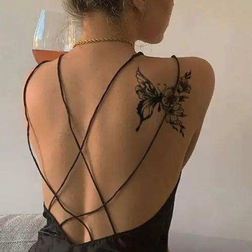 Back view of woman with butterfly tattoo wearing criss-cross dress, holding glass of wine.