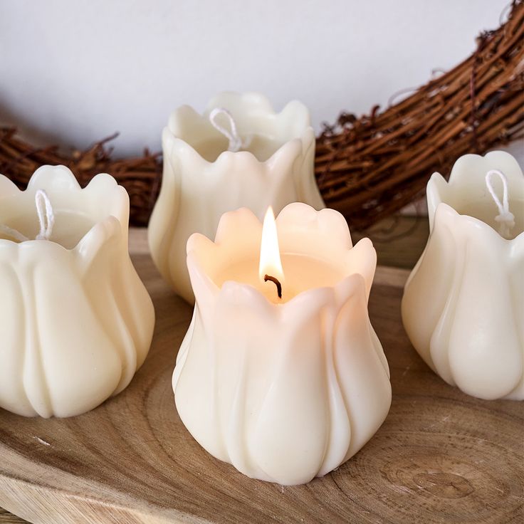 White flower-shaped candles on wood, with one lit. Cozy home decor ambiance.