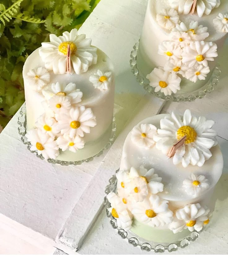 Decorative white floral cakes with daisy designs on glass stands, perfect for weddings or spring celebrations.