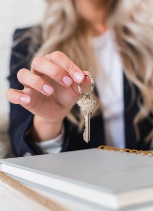 Woman holding a key above a notebook, symbolizing new opportunities or real estate transactions.