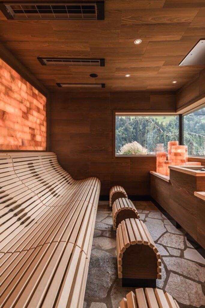 Modern wooden sauna interior with sloped benches, soft lighting, and a window view of lush green trees.