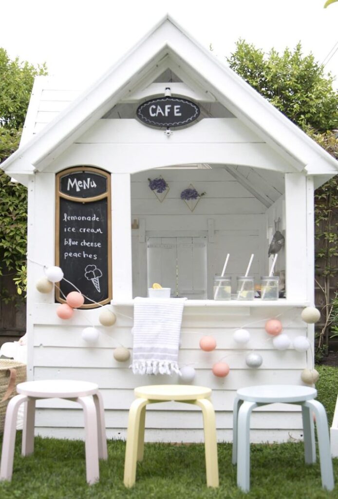 Charming backyard cafe setup with menu board, pastel stools, and decorative lights. Cozy outdoor refreshment stand.