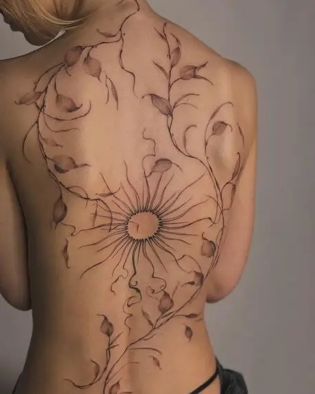 Back tattoo with abstract sun and vine design on a person's bare skin.