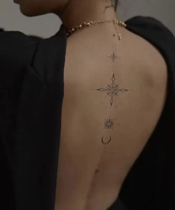 Elegant geometric tattoo design on woman's back, featuring stars and crescent moon, wearing black blouse.