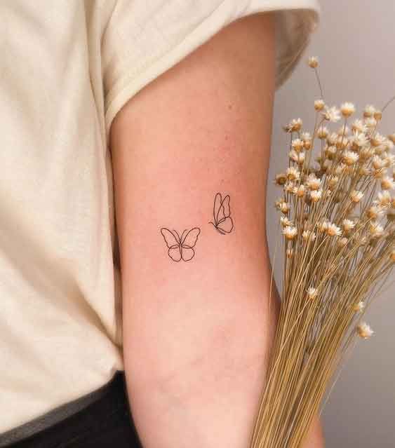 Minimalist butterfly tattoos on arm holding dried flowers, showcasing simple and elegant tattoo art.