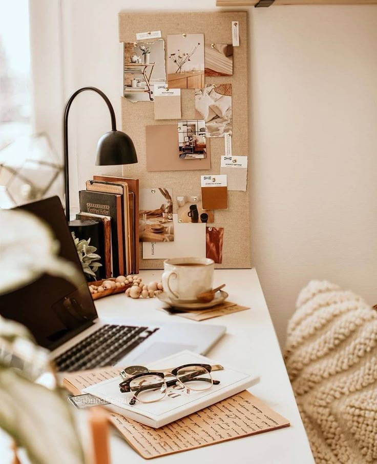 Cozy home office with laptop, coffee, and inspiration board on a white desk, styled with warm neutral tones.