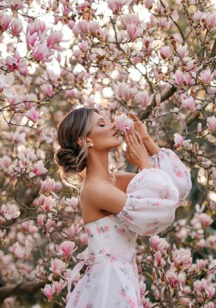 Woman in floral dress enjoying blooming magnolia tree in spring garden.