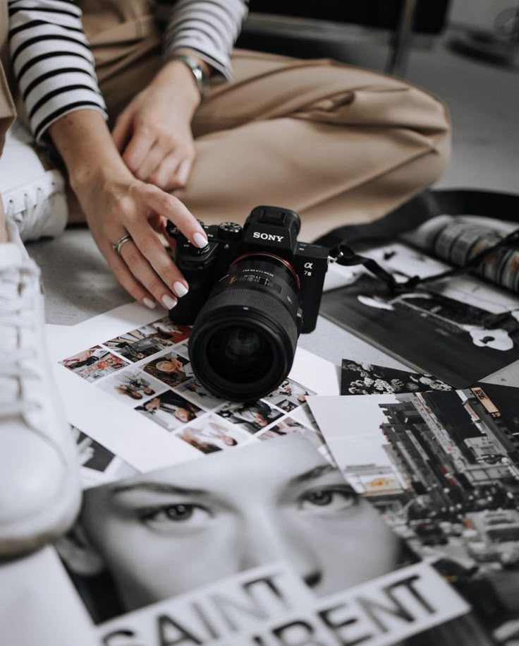 Person holding a Sony camera, surrounded by black and white photos on the floor.