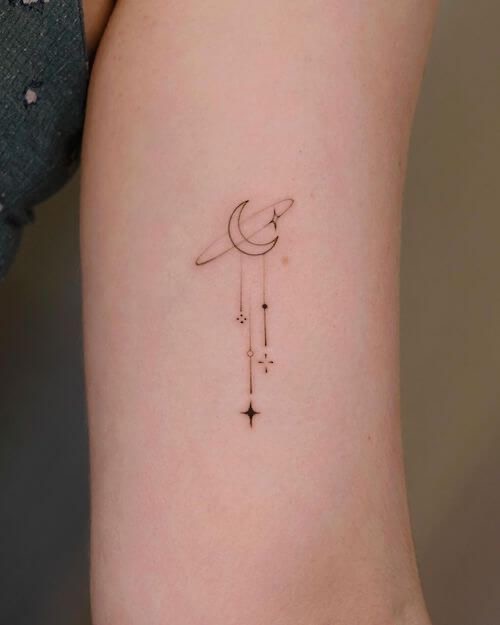 Minimalist arm tattoo with crescent moon, stars, and dots, featuring delicate line art design.